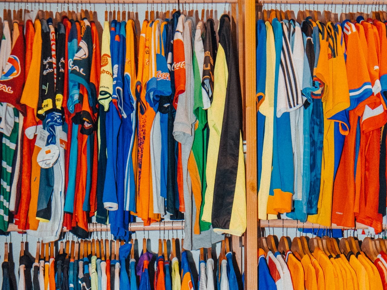 A wall of soccer jerseys hanging on wooden hangers in a closet rack
